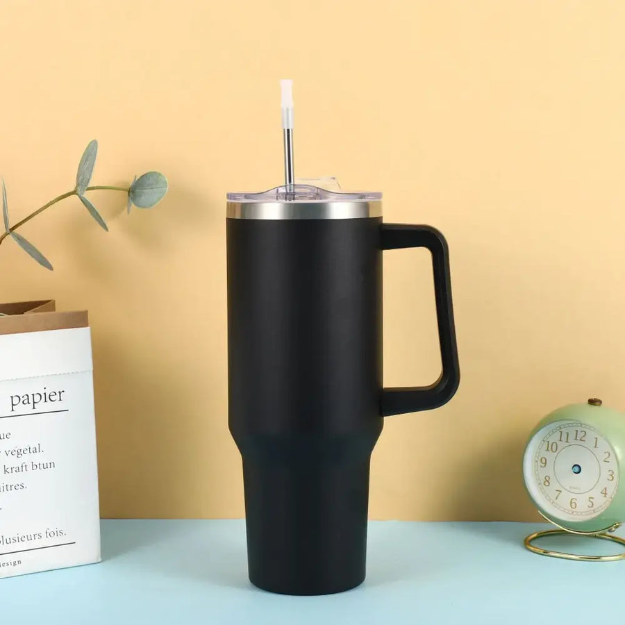 Black matte-finish insulated tumbler with a stainless steel rim, handle, and clear lid featuring an integrated straw.