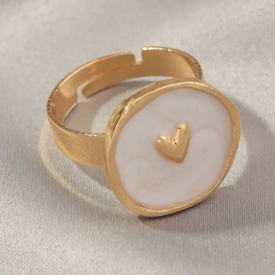Gold-toned adjustable ring with a round, off-white enamel face featuring a small gold heart in the center.