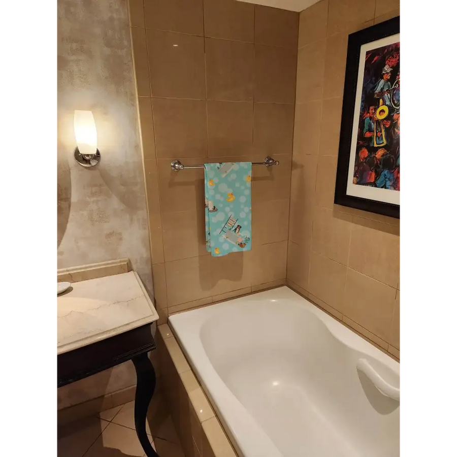A light blue towel with a playful pattern of yellow ducks and small boats hangs neatly on a chrome towel rack.