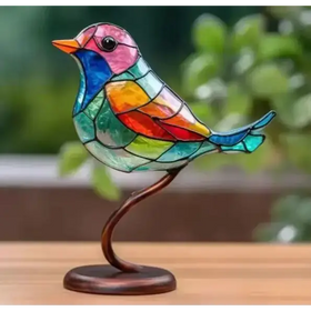 A vibrant, multicolored stained glass bird figurine with a pink head, orange beak, and rainbow-patterned body mounted on a curved bronze stand.