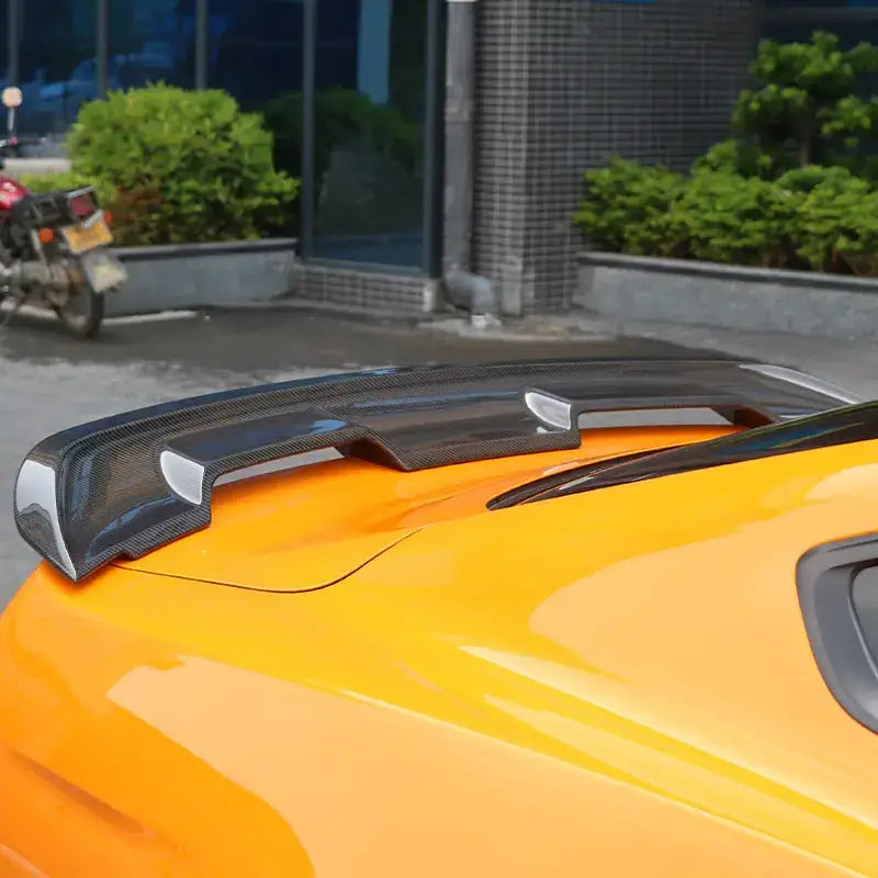 Black carbon fiber rear spoiler with sleek, aerodynamic design mounted on a vibrant orange sports car.