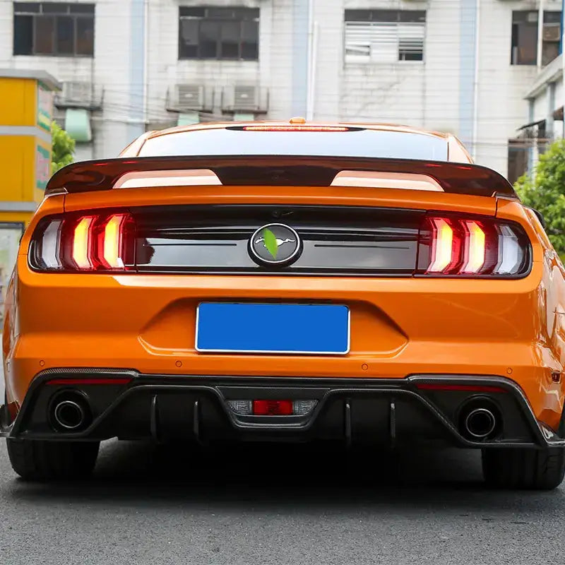 Vibrant orange ford mustang with a black rear spoiler and dual exhaust system.