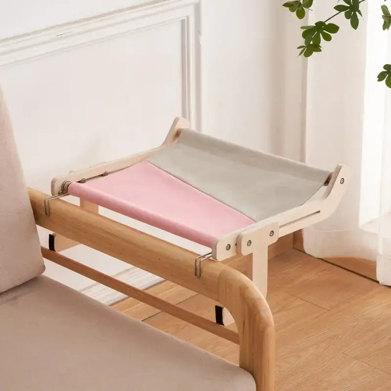 A minimalist wooden cat bed with a pink and gray fabric sling.