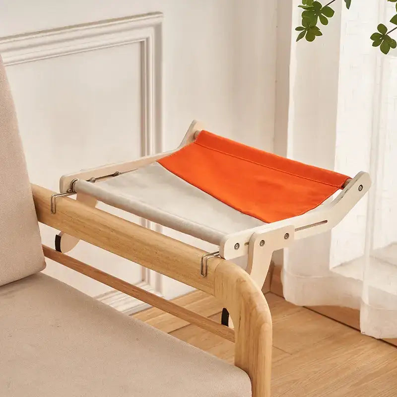 A cozy, two-toned cat bed with a light beige and vibrant orange fabric sling supported by a minimalist wooden frame.