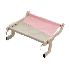 A minimalist wooden pet bed with a two-tone fabric top—soft pink on one side and beige on the other—and black rubber feet for stability.