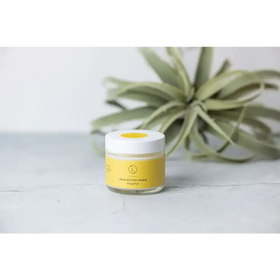 A clear glass jar with a white lid and yellow label, containing grapefruit-scented shea butter cream.