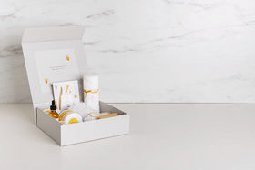 White gift box with gold accents, containing a curated set of bath and body products.