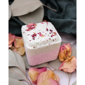 A square-shaped bath bomb with a gradient from white to pink, topped with dried rose petals.