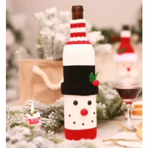 A festive red and white knitted wine bottle cover designed to look like a snowman, complete with black hat trim, green holly accents, and a cheerful face.