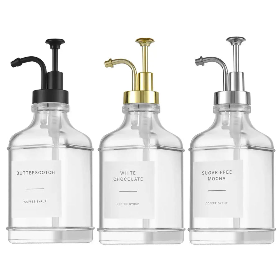Three clear glass syrup dispensers with black, gold, and silver pump tops.