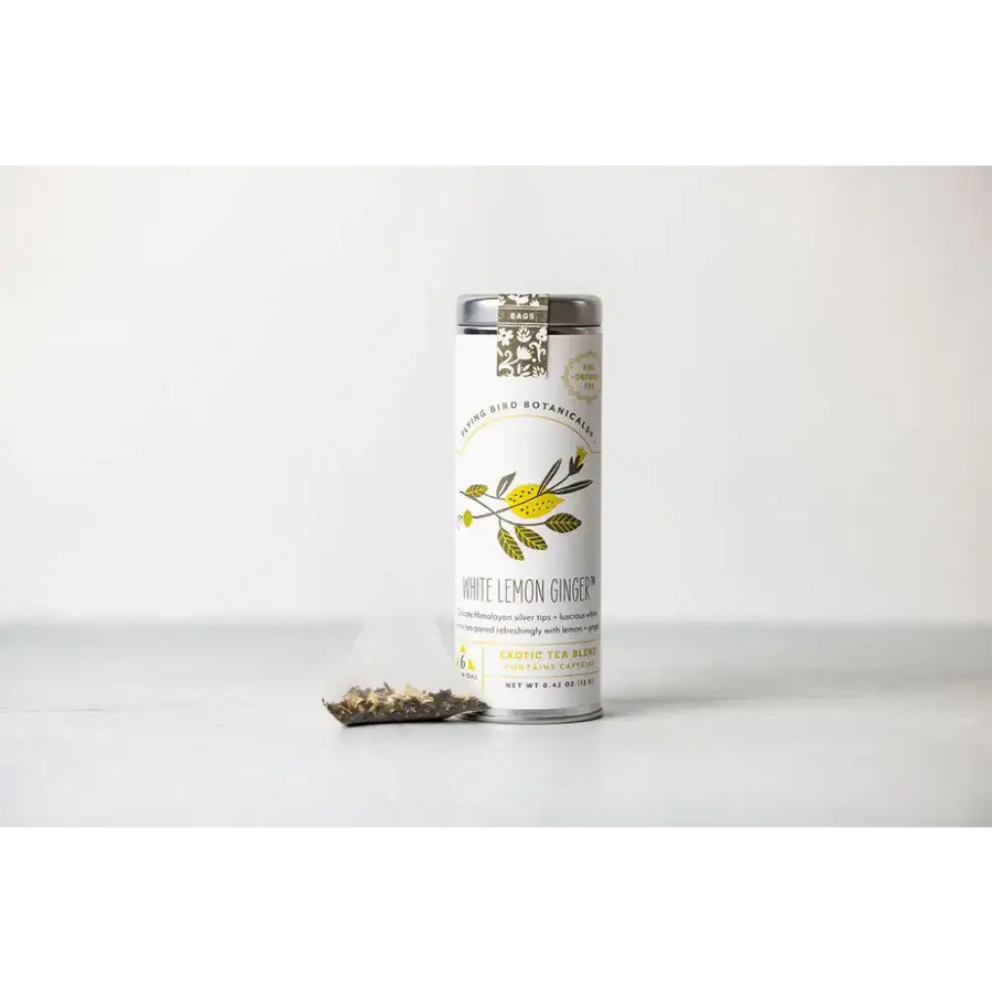 A sleek white cylindrical tin with a silver lid and botanical illustrations, labeled ’white lemon ginger’ by living bird botanica.
