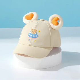 Beige baseball cap with plush bear ears and embroidered teddy bear in a ufo, featuring ’happy’ text.