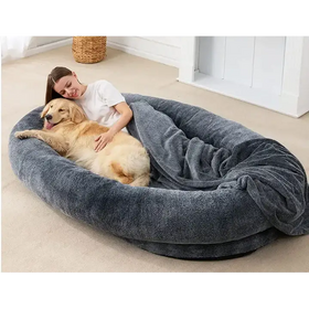 Plush gray oval dog bed with soft textured fabric and a cozy blanket draped over the edge