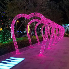 A series of glowing pink heart-shaped light arches, each constructed from a framework wrapped in sparkling led lights.