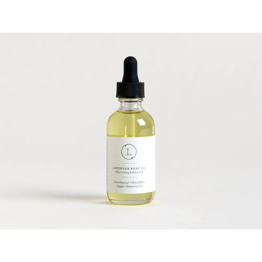 A clear glass bottle with a black dropper cap contains pale yellow lavender body oil, labeled as ’100% natural • non-gmo • vegan • essential oil.’