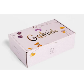 A delicate lavender-colored cardboard box adorned with gold foil lettering and a floral design featuring purple and yellow blossoms.