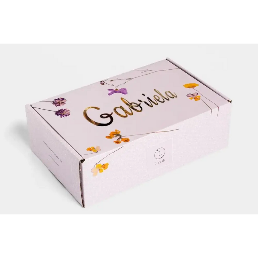 A delicate lavender-colored cardboard box adorned with gold foil lettering and a floral design featuring purple and yellow blossoms.