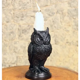 Black owl-shaped candle holder with a white wax candle lit atop its head.