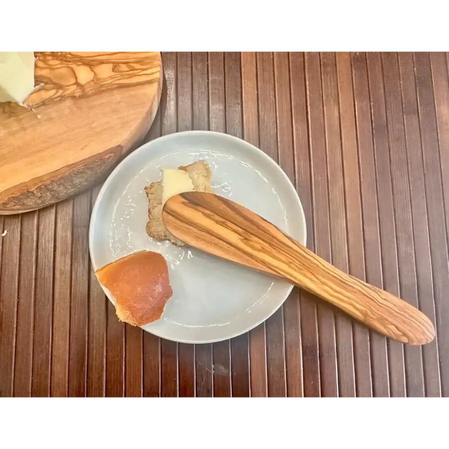 A sleek olive wood butter knife with a natural, striped grain pattern rests on a light gray plate.