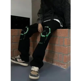 Black jeans with green embroidered skull designs on the knees.