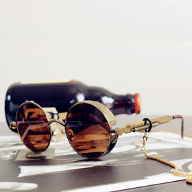 Golden-framed round sunglasses with amber-tinted lenses and a chain strap.