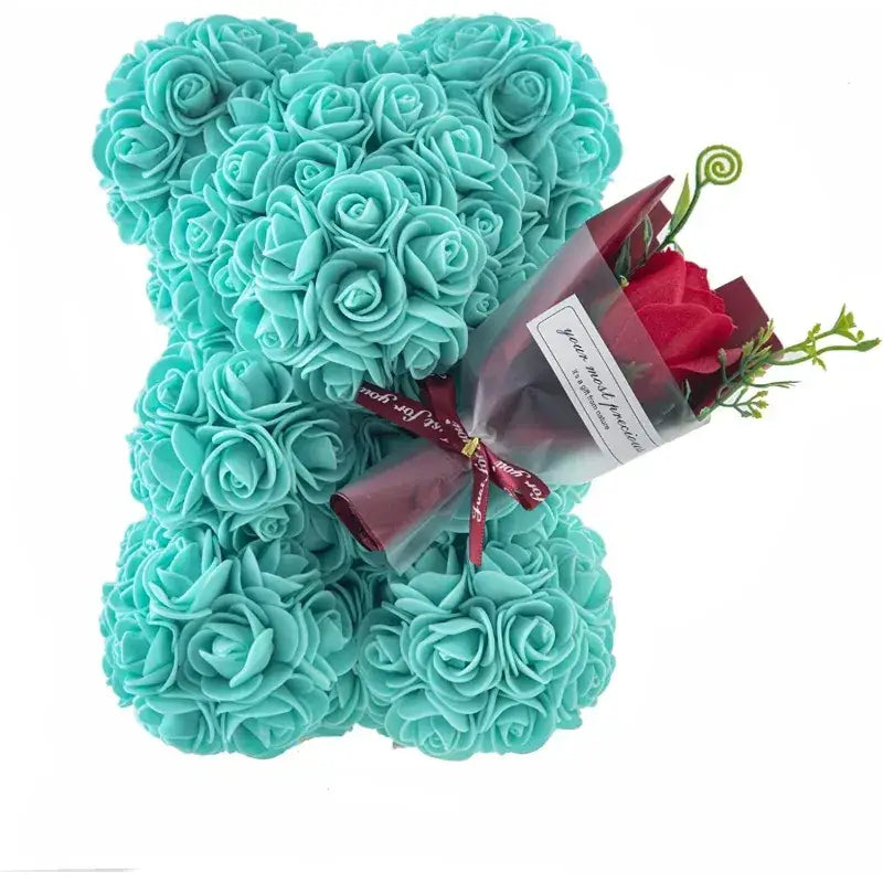 A turquoise rose-covered bear figurine holding a bouquet of red roses wrapped in maroon paper.