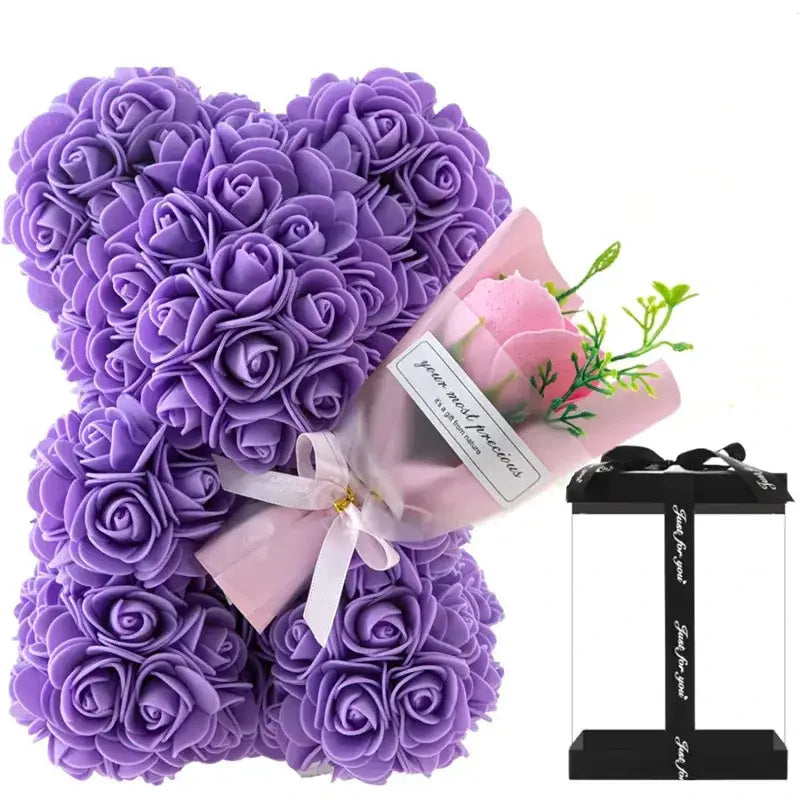 Purple rose-covered teddy bear with a small pink bouquet and gift box beside it.