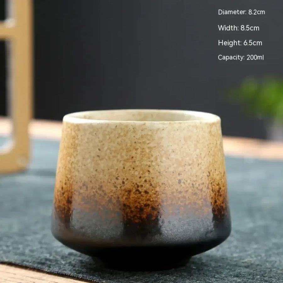 A handcrafted ceramic teacup with a gradient glaze transitioning from light beige to deep brown at the base, featuring subtle speckles and an organic, rustic design.