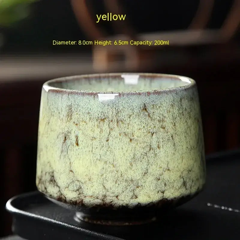 A handcrafted ceramic tea cup with a mottled green and brown glaze, featuring a slightly flared rim and a sturdy base.