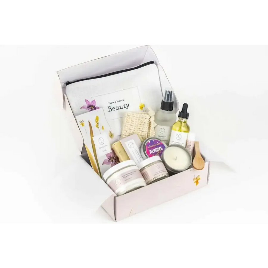 A pale pink gift box filled with assorted natural beauty products, including candles, lotions, and essential oils.