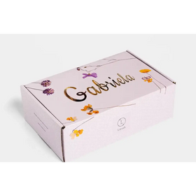 A delicate lavender-colored cardboard box adorned with gold foil lettering and a floral design featuring purple and yellow blossoms.