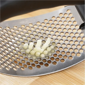 Silver metal garlic press with a perforated surface and small, peeled cloves of garlic resting on it.