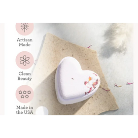 A lavender heart-shaped bath bomb with dried flower petals embedded in its surface.