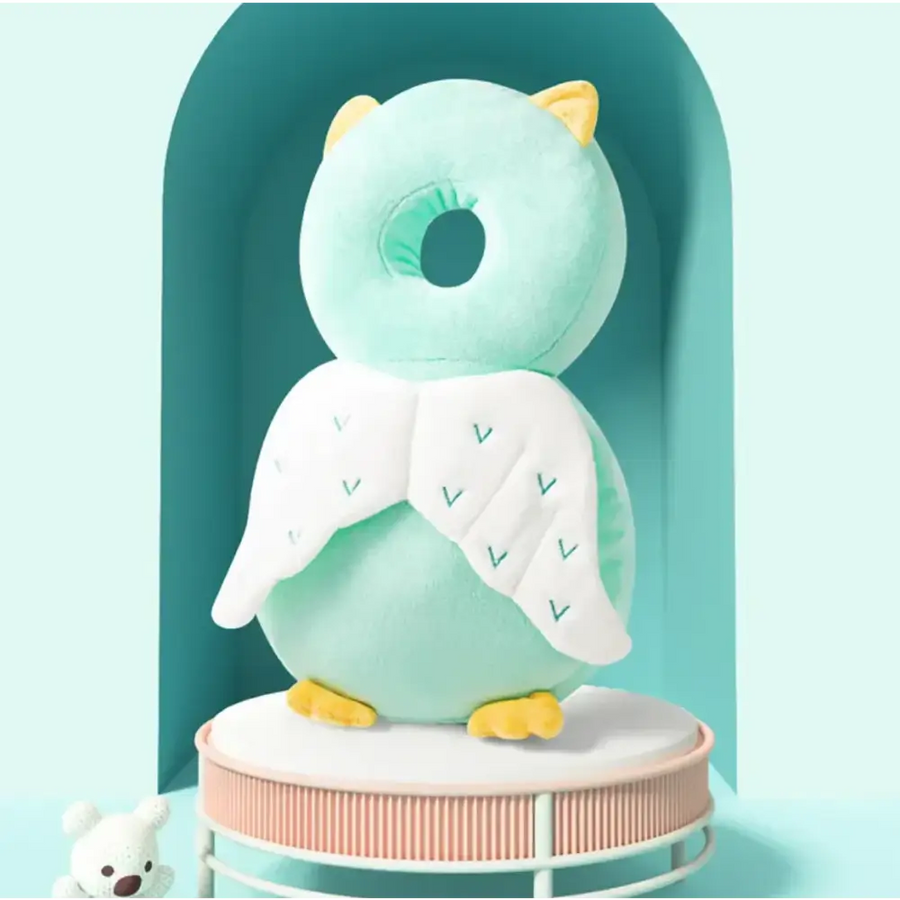 A soft mint green plush owl-shaped baby back support with white angel wings embroidered with teal chevrons and yellow feet.