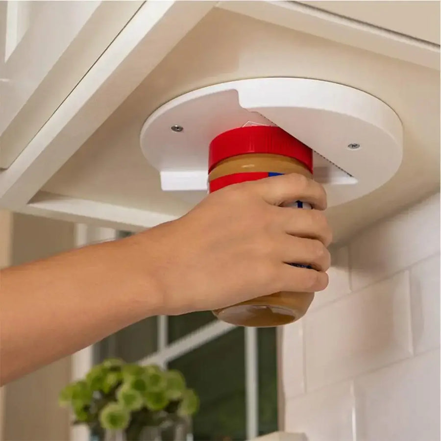 White circular jar opener mounted under a cabinet, holding a red-lidded peanut butter jar.