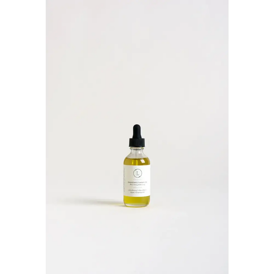 A clear glass bottle with a black dropper cap contains golden-yellow grape seed body oil, labeled ’nourishing & moisturizing’ on its white label.