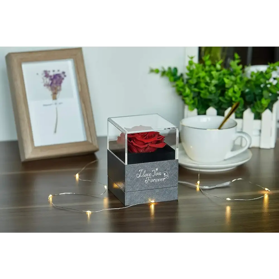 A vibrant red preserved rose nestled inside a clear acrylic cube with a textured gray base that reads ’i love you forever.’