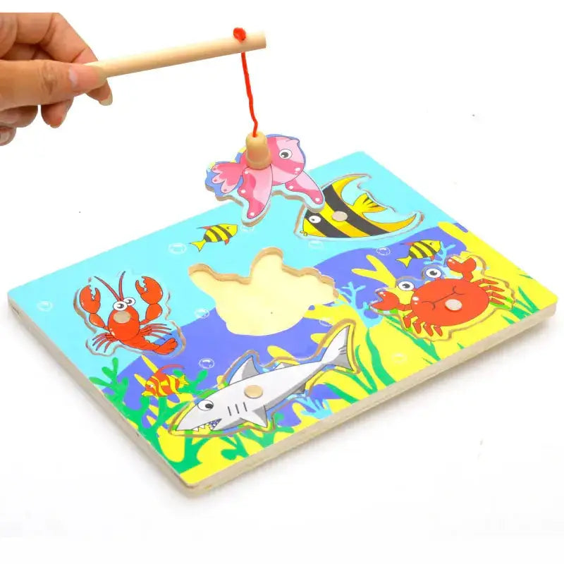 Colorful wooden magnetic fishing game board with cartoon sea creatures and a pink fish-shaped magnet on a stick.
