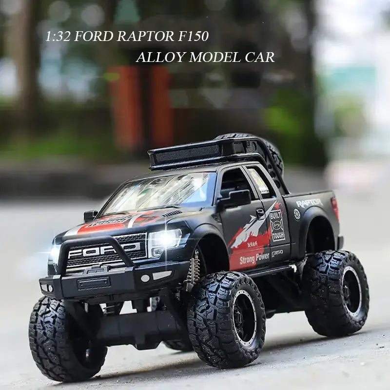 Black 1:32 scale alloy model of a ford raptor f-150 pickup truck with red and white decals, rugged tires, and roof rack.