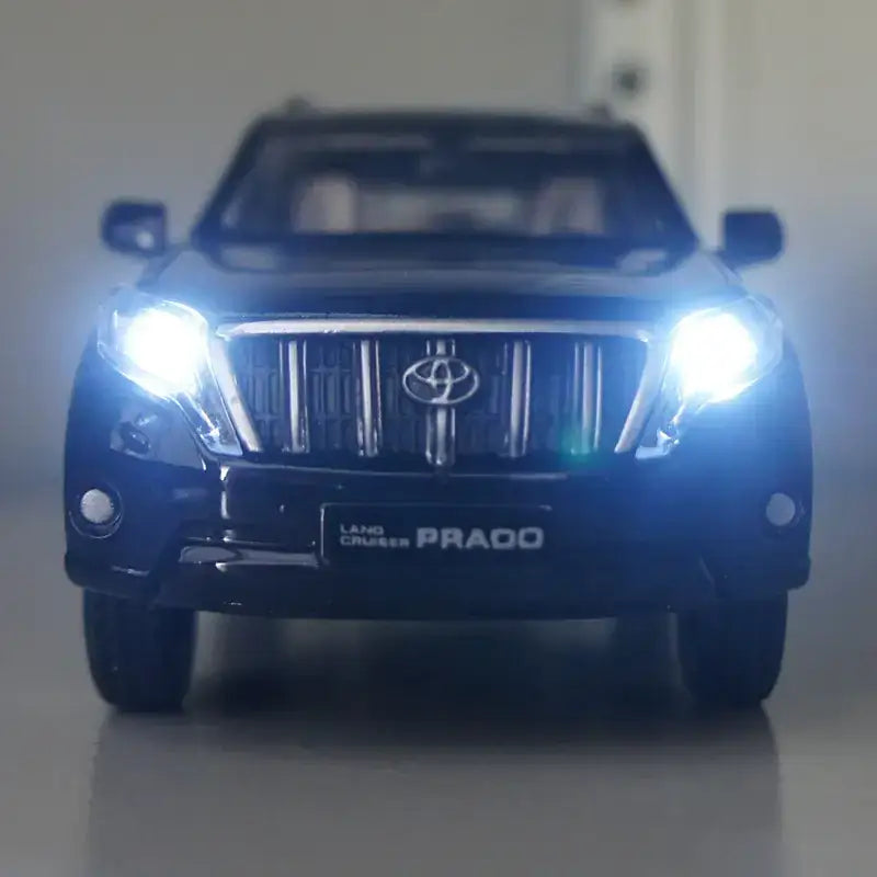 Black die-cast toyota land cruiser prado model toy with illuminated headlights and chrome grille.