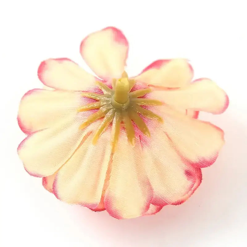 A delicate artificial flower with soft cream-colored petals edged in pink and a yellow center, crafted from fabric-like material.