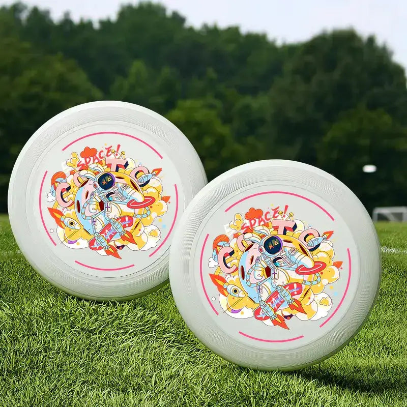 Two white plastic frisbees with colorful cartoon astronaut designs and pink circular borders.
