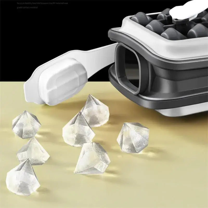 Clear, faceted diamond-shaped ice cubes scattered on a surface next to an open gray and white collapsible ice cube tray.