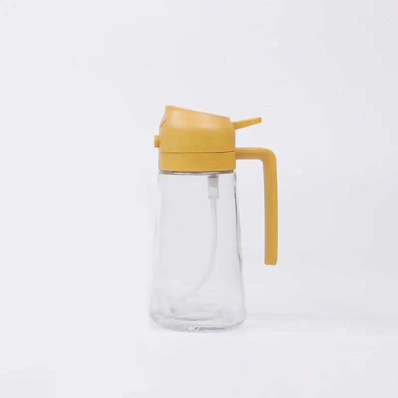 Clear glass oil dispenser with a mustard-yellow plastic lid and handle.