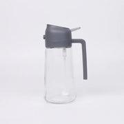 Clear glass oil dispenser with a matte gray plastic lid and handle.
