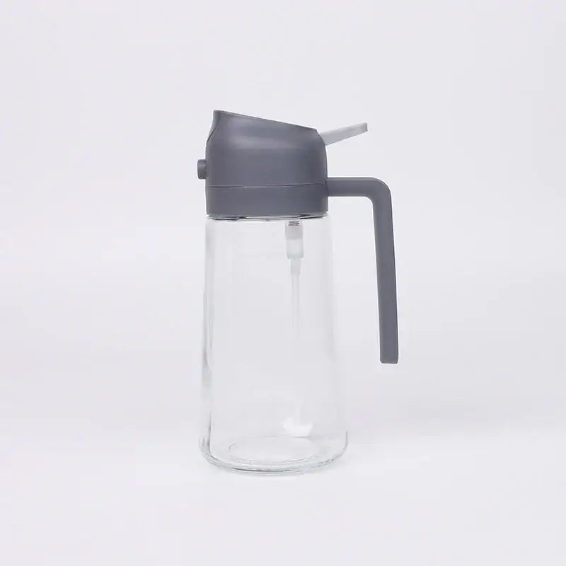 Clear glass oil dispenser with a matte gray plastic lid and handle.