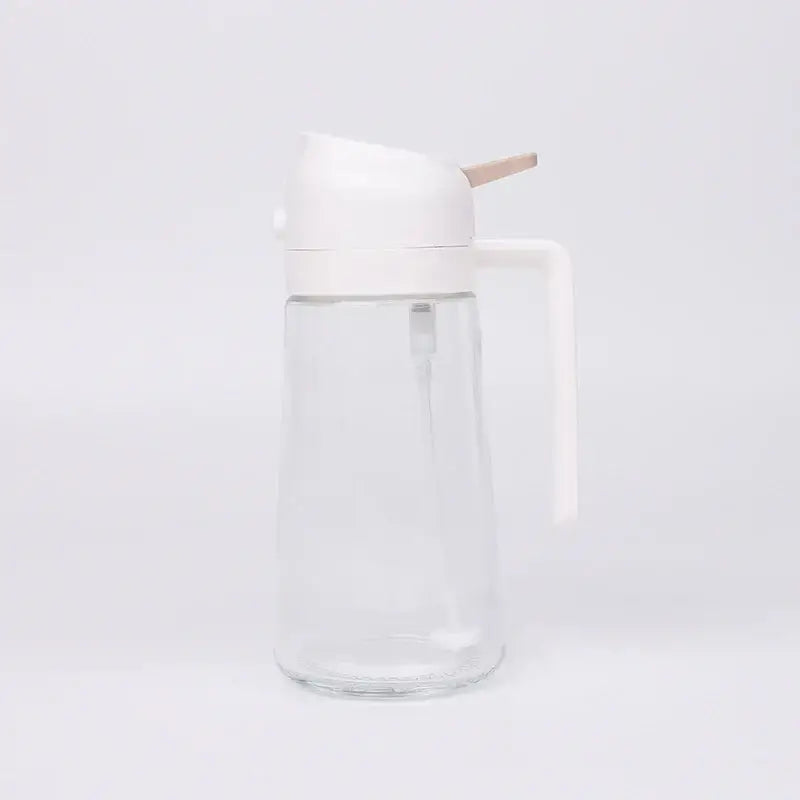 Clear glass oil dispenser with a white plastic lid and handle, featuring a wooden spout for controlled pouring.