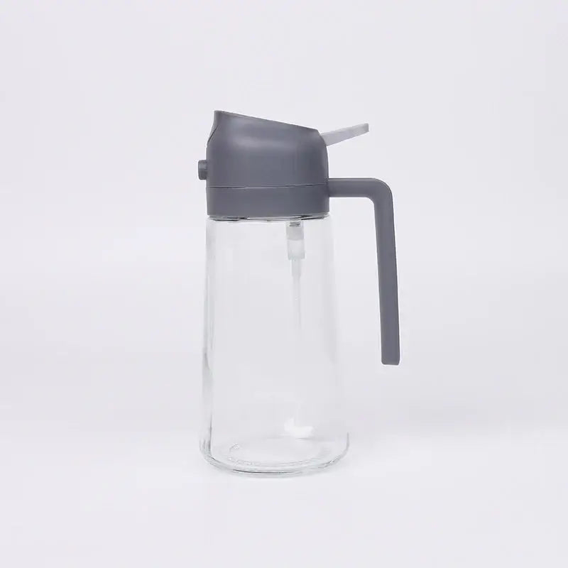 Clear glass oil dispenser with a gray plastic lid and handle.