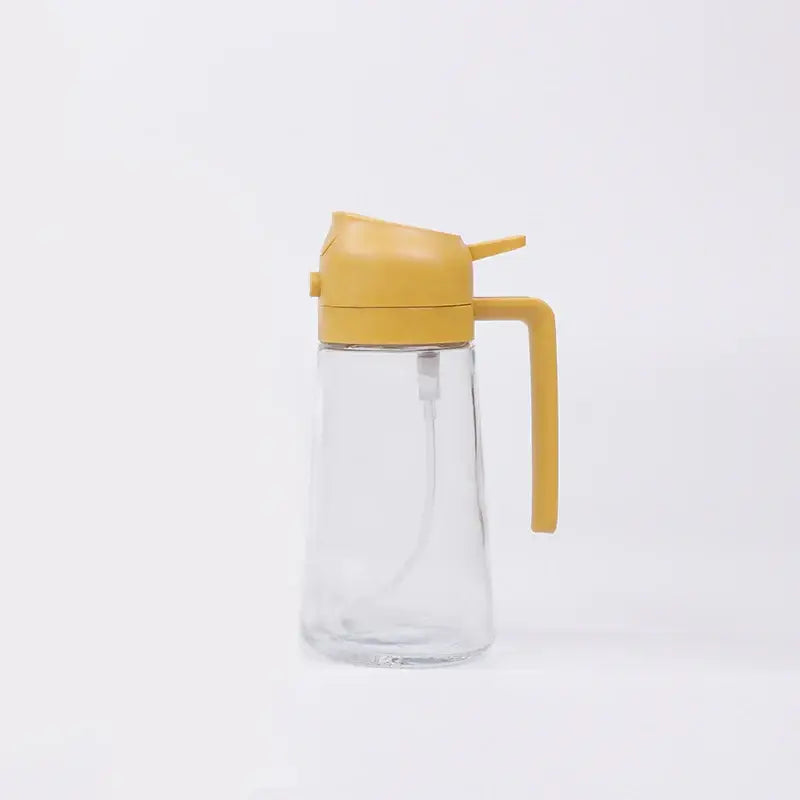 Clear glass oil dispenser with a mustard-yellow plastic lid and handle.