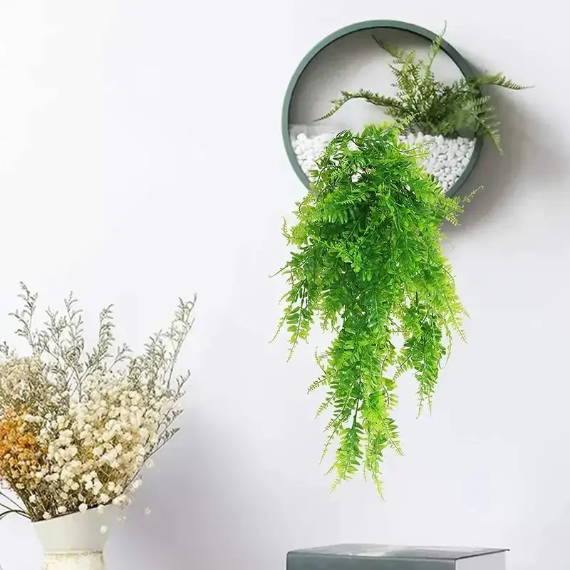 Green artificial fern hanging from a circular wall-mounted planter with white pebbles inside.
